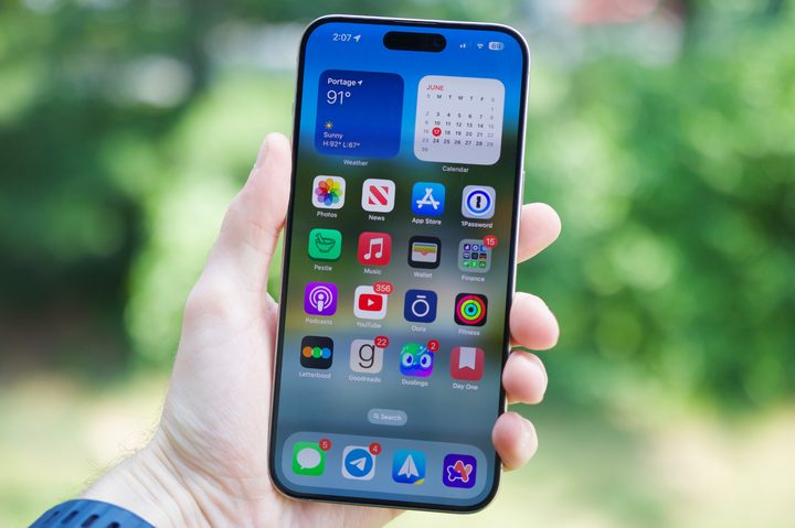 Someone holding an iPhone 15 Pro Max with the screen on and showing the home screen.