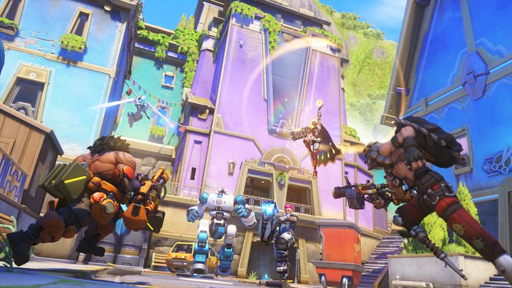 A bunch of Overwatch heroes running around the Runapasi map, specifically in front of a tall purple building with blue ones on either side.