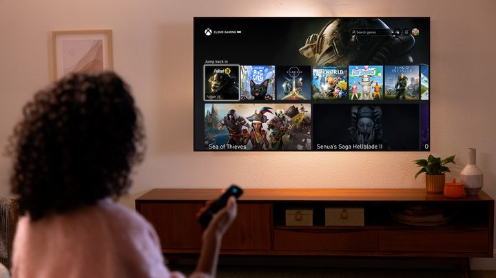 A woman holding a remote while looking at an Amazon Fire TV with the Xbox app on it. It's on the Cloud Gaming menu with Fallout 76, Senua's Saga Hellblade 2 and more on it.