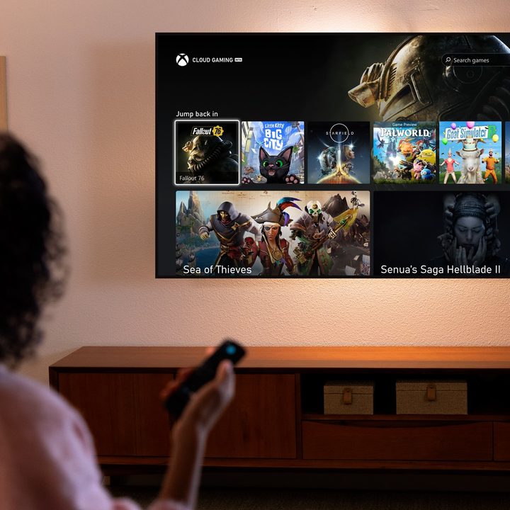 A woman holding a remote while looking at an Amazon Fire TV with the Xbox app on it. It's on the Cloud Gaming menu with Fallout 76, Senua's Saga: Hellblade 2, and more on it.