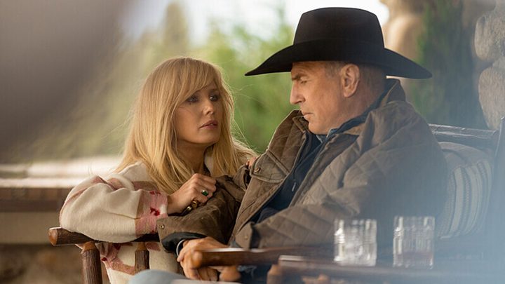 A woman knees beside her father who is sitting outside with a cowboy hat on Yellowstone.