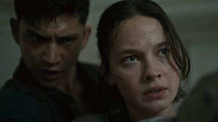 A girls holds a gun with a man looking behind her head.
