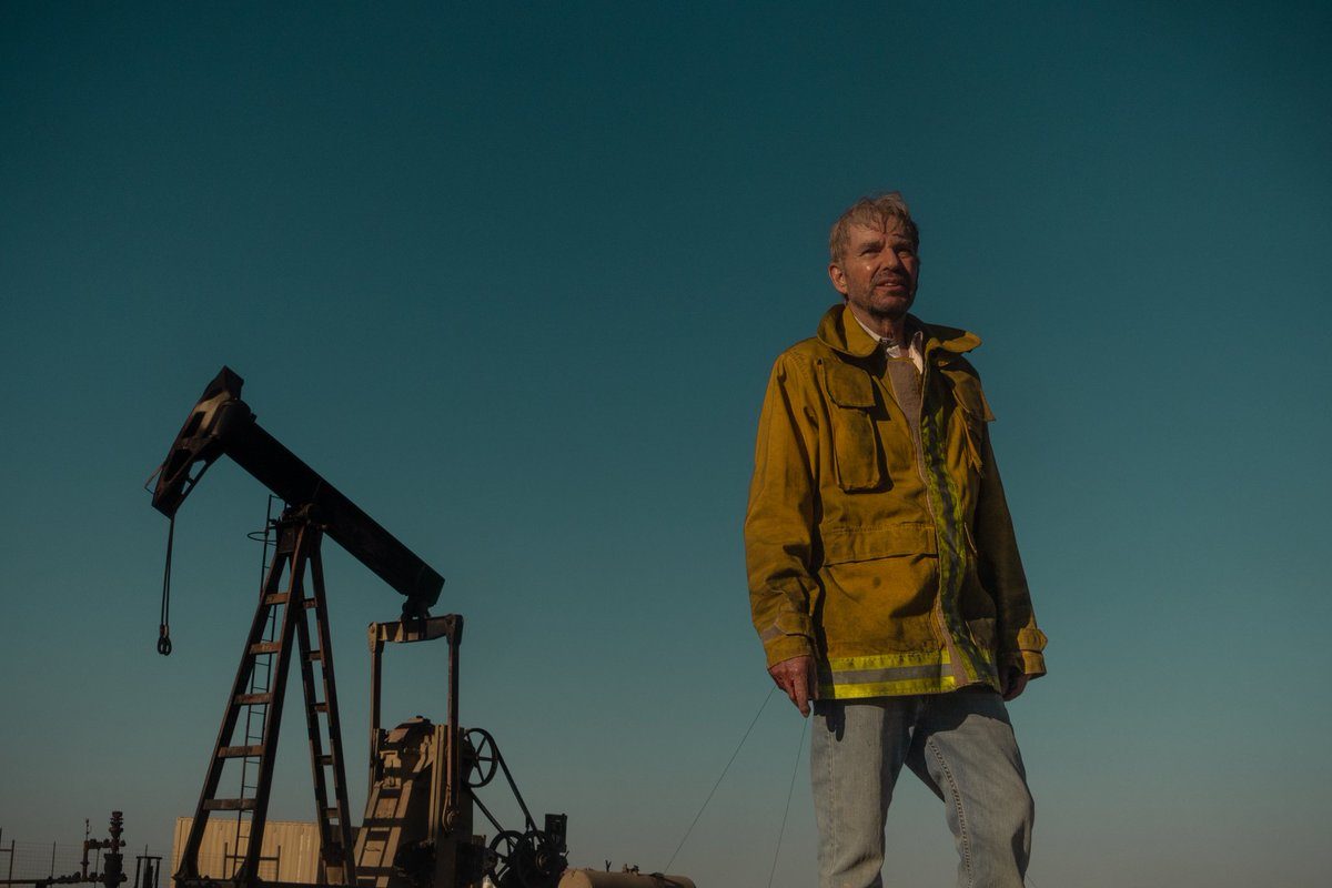 A man stands in front of an oil field and stares.