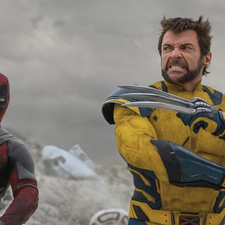 A masked Ryan Reynolds watches as Hugh Jackman poses with his claws in a still from the movie Deadpool & Wolverine
