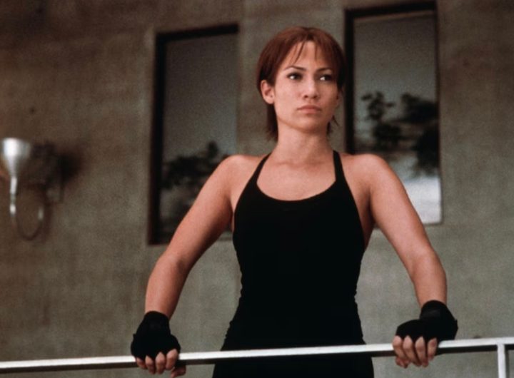 Jennifer Lopez stands up and holds a metal bar.