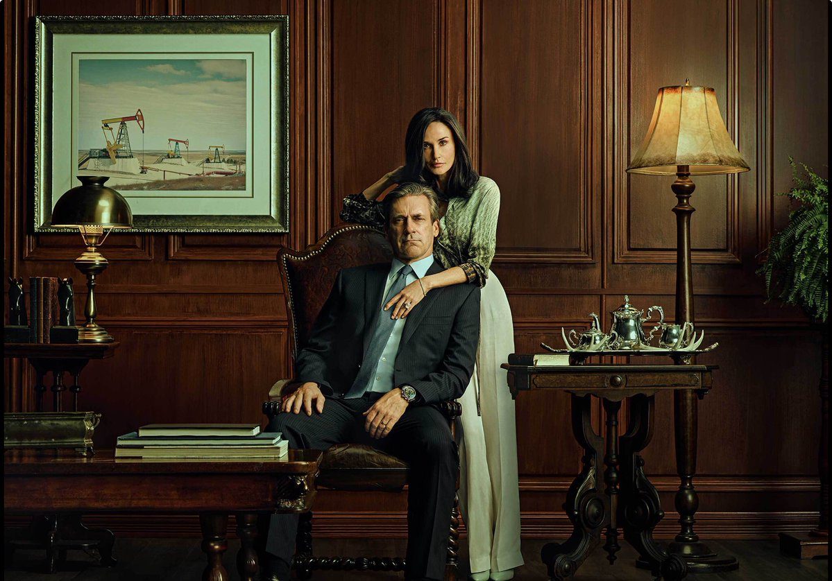 A man sits down on a chair with a woman holding onto his shoulders.