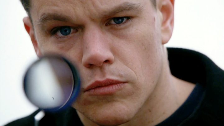 Matt Damon as Jason Bourne looking directly at the camera while holding a sniper rifle in The Bourne Supremacy.
