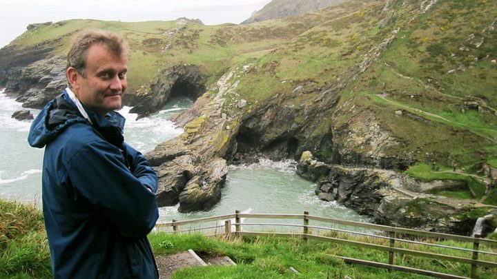 Hugh Dennis standing in front of the British coast.