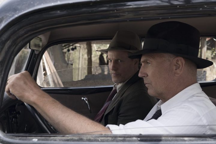 Kevin Costner sits behind the wheel while Woody Harrelson stares at him in front seat.