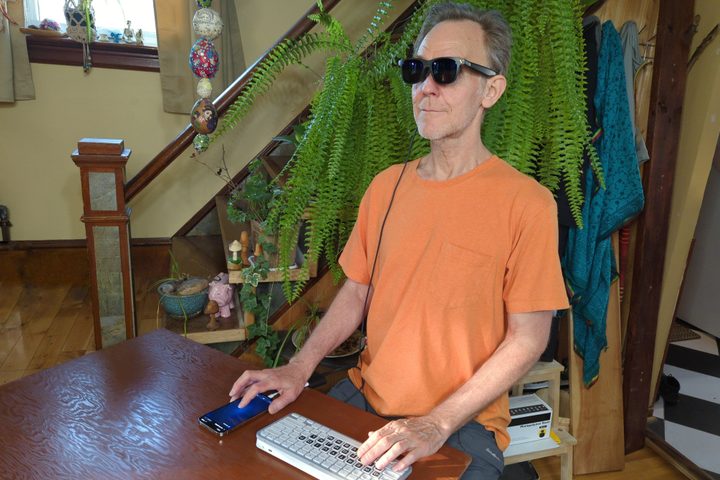 Alan Truly wears Viture Pro smart glasses while working with an iPhone and Bluetooth keyboard.