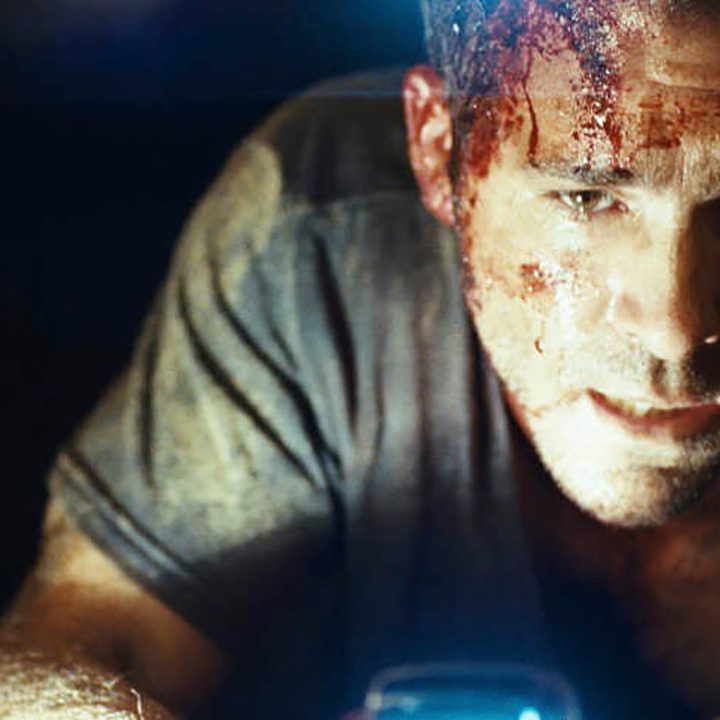 Ryan Reynolds in a dark coffin shining a light on his bloodied face in Buried.