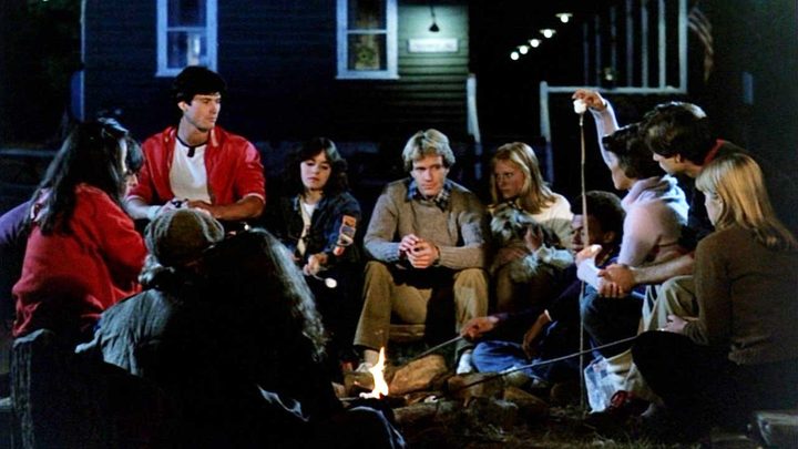 A group of teens sit around a campfire in Friday the 13th Part Two.
