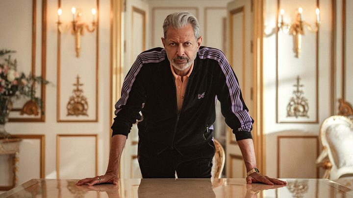 Jeff Goldblum looking straight ahead leaning over a counter with both hands on it in a scene from Kaos on Netflix.