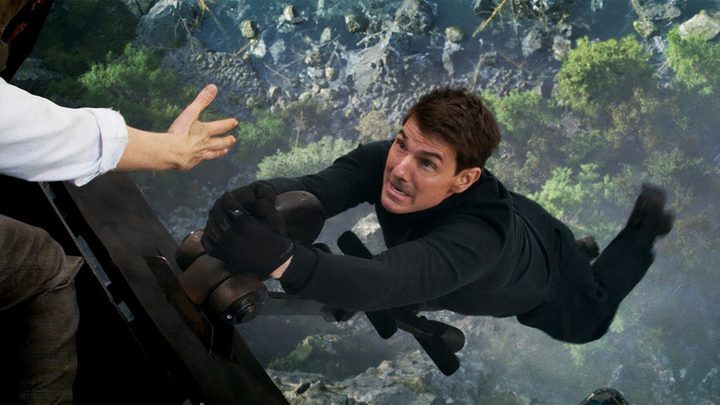 Tom Cruise hanging from a ledge screaming with a hand trying to grab him in a scene from Mission: Impossible - Dead Reckoning Part One.