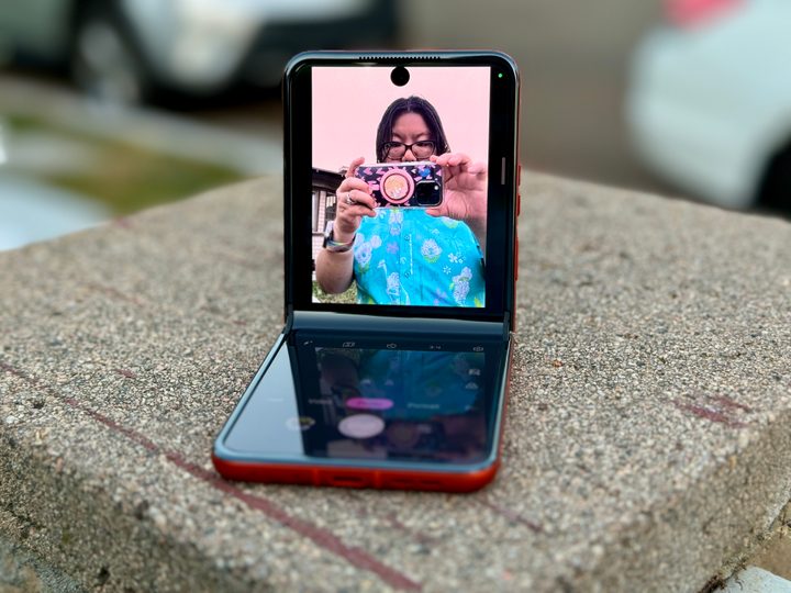 Motorola Razr 2024 in Spritz Orange propped open in a partial fold to show using the selfie camera.
