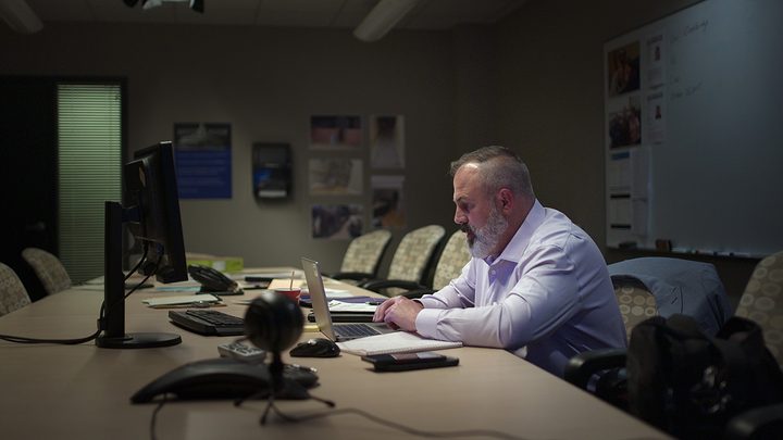 A police officer sits at his desk working on a computer in a scene from Unsolved Mysteries season 4 on Netflix.