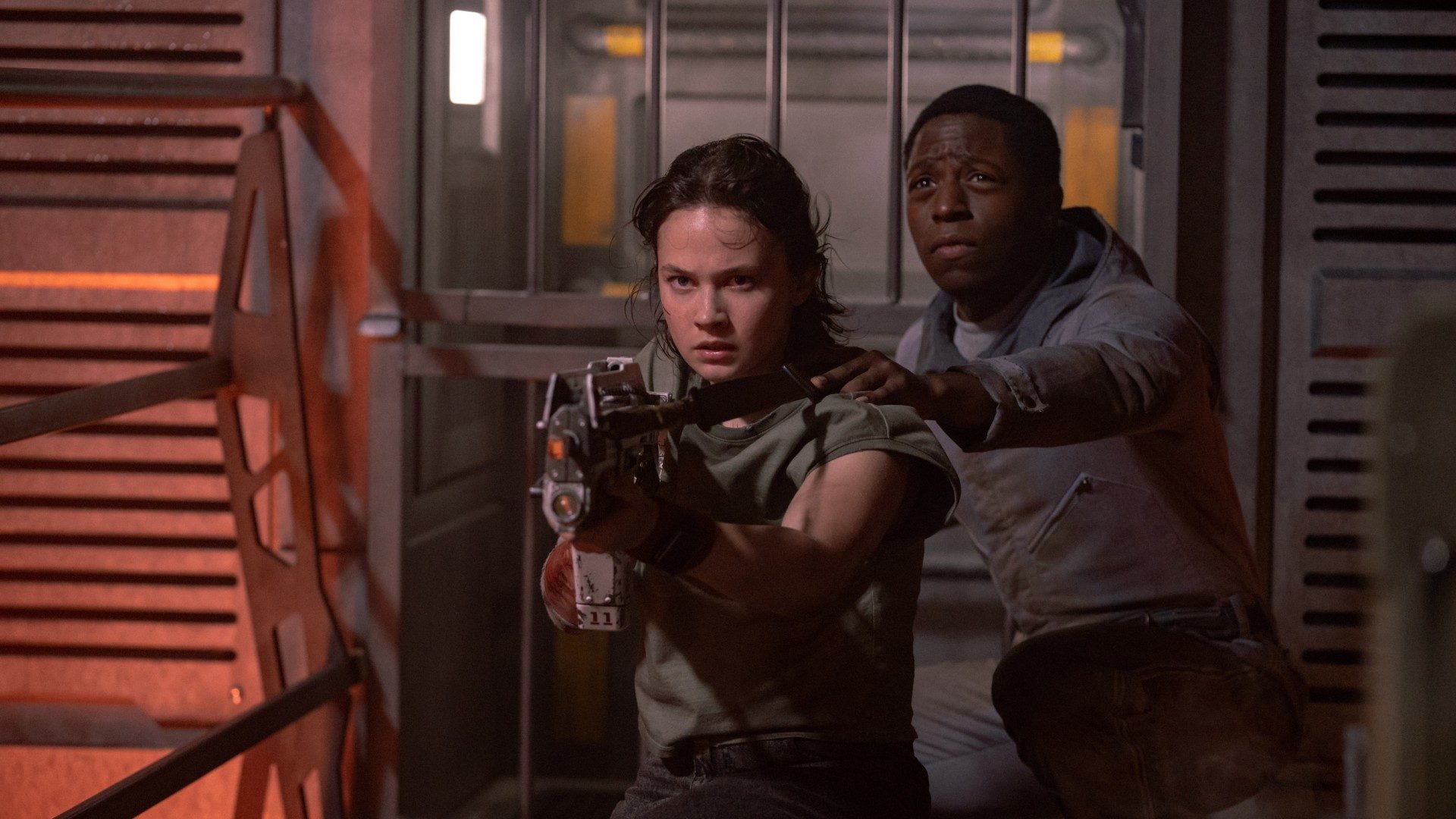 Cailee Spaeny aims a gun as David Jonsson stands behind her in a still from the movie Alien: Romulus.