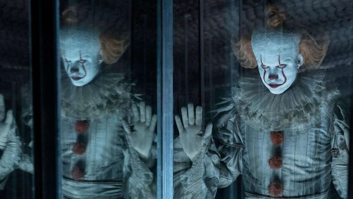 Bill Skarsgård as Pennywise the Dancing Clown pressing his hands against a mirror in It Chapter Two,