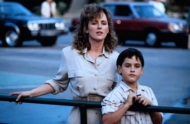 A woman stands behind a rail with her young son and stares.