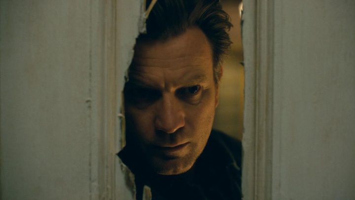 Ewan McGregor as Danny Torrance looking through a broken door frame in Doctor Sleep.
