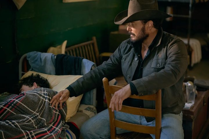 A man sits on a chair and leans toward someone in a bed.