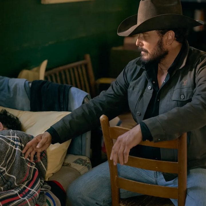 A man sits on a chair and leans toward someone in a bed.
