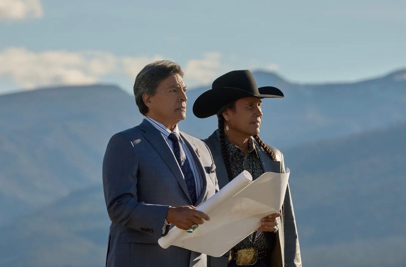 A man holds a folder in his hands while standing next to someone else.