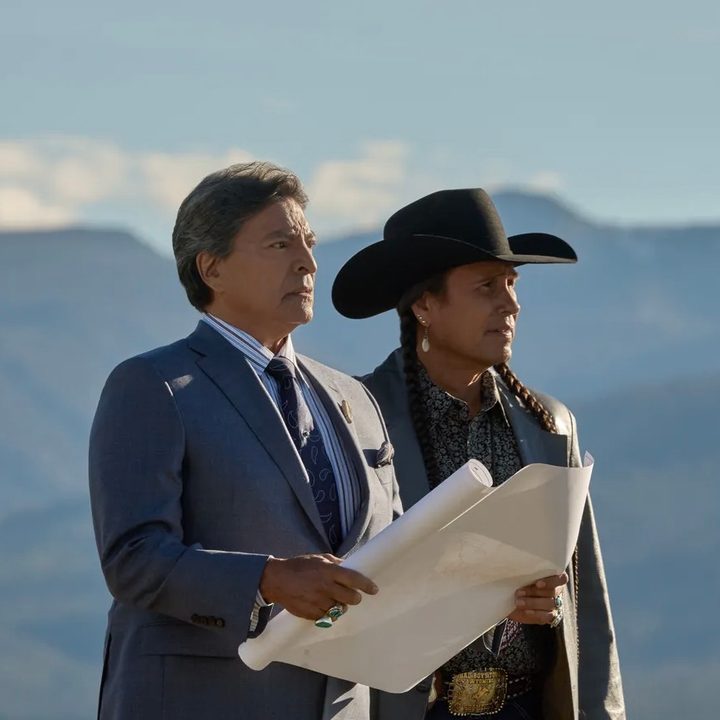 A man holds a folder in his hands while standing next to someone else.
