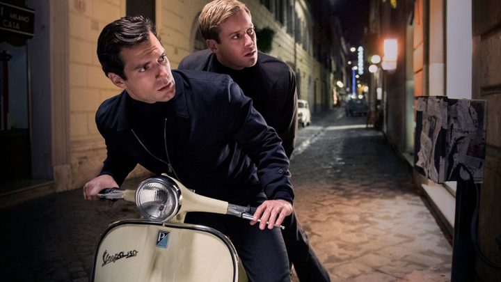 Henry Cavill and Armie Hammer as Napoleon Solo and Ilya Kuryakin on a Vespa looking to their left in The Man From UNCLE.