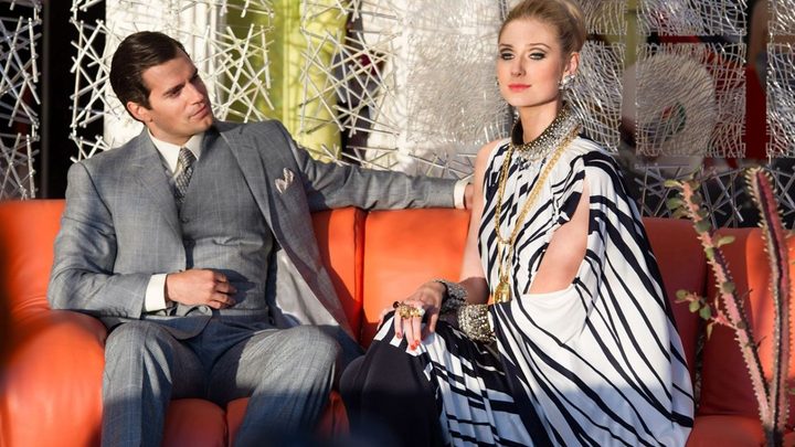 Henry Cavill and Elizabeth Debicki as Napoleon Solo and Victoria Vinciguerra ona couch at a party in The Man From UNCLE.