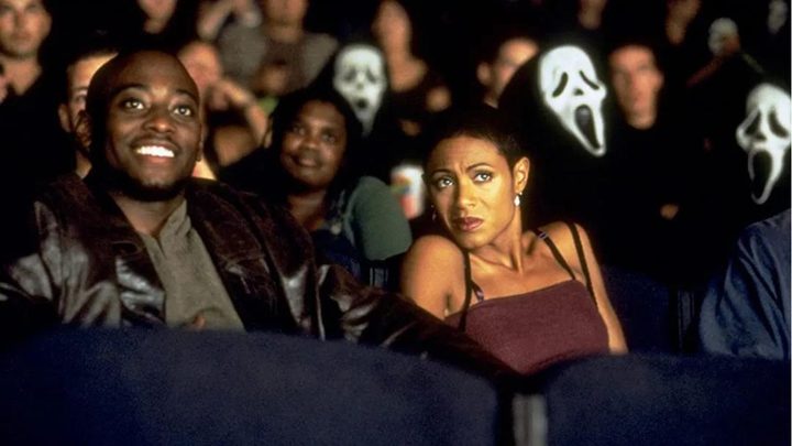 Omar Epps and Jada Pinkett as Phil and Maureen at a movie theater surrounded by people with Ghostface masks in Scream 2.