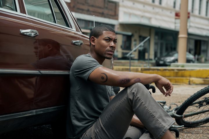 A man sits by a car in Rebel Ridge.