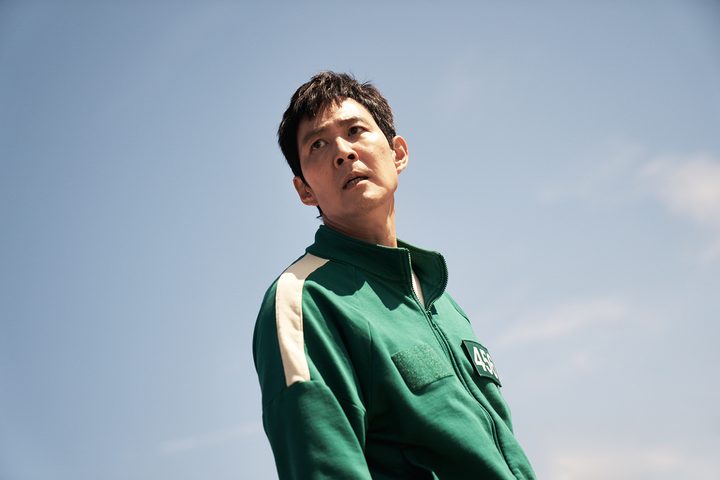 A man in a green track suit poses and stares.