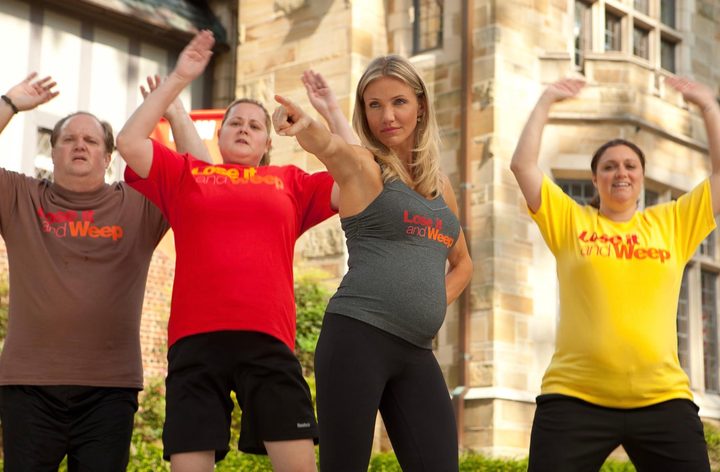 A pregnant Cameron Diaz points a finger while people jump behind her.