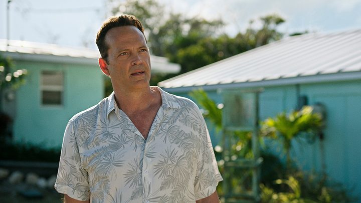 Vince Vaughn in a floral button top standing by a beach house looking annoyed in a scene from Bad Monkey.