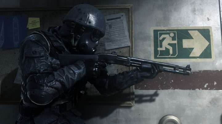 A man in black armor holding a shotgun and leaning against a wall.