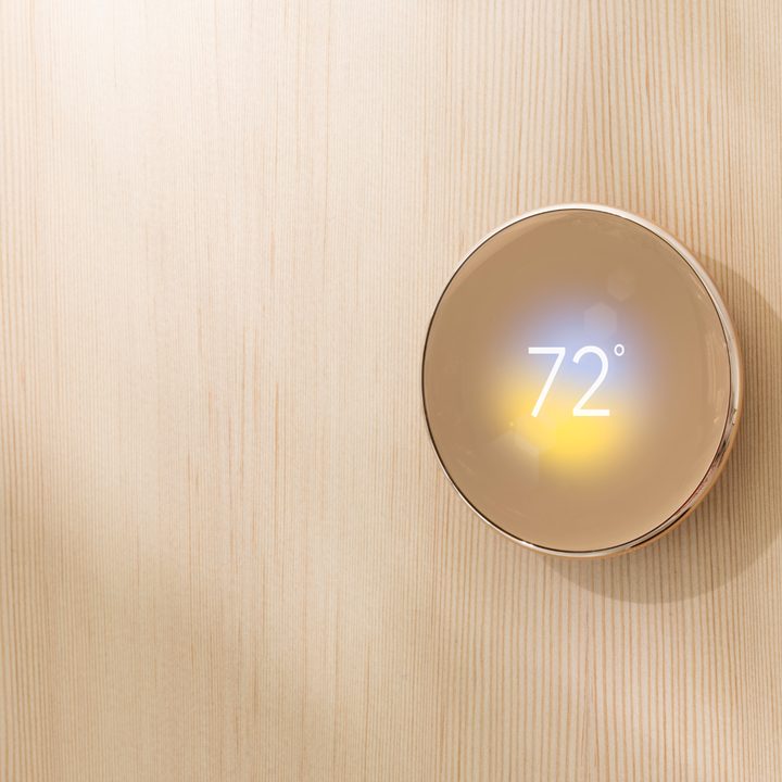 Google Nest Learning Thermostat (4th Gen) on a wood wall.