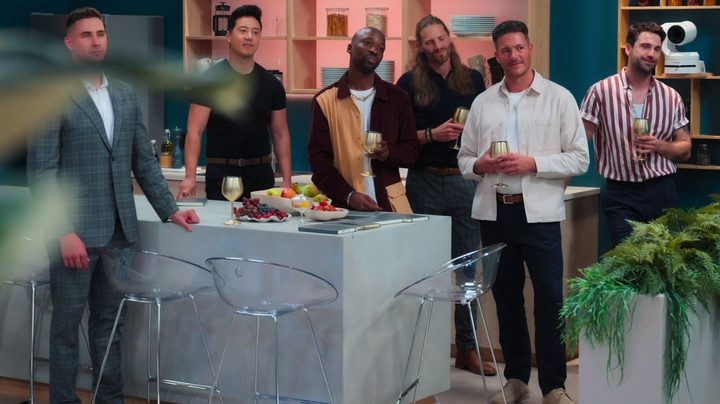 The men from Love is Blind: UK in their suite standing around listening to the hosts.