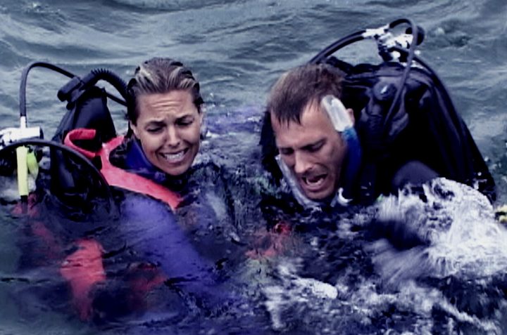 A man and a woman look at something in the water in Open Water.