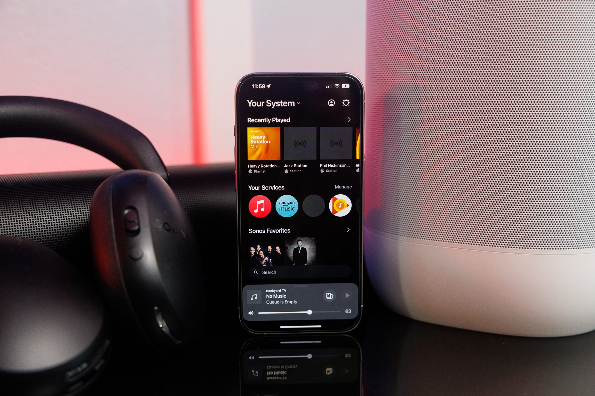 The Sonos app on an iPhone in front of Sonos speakers and headphones.