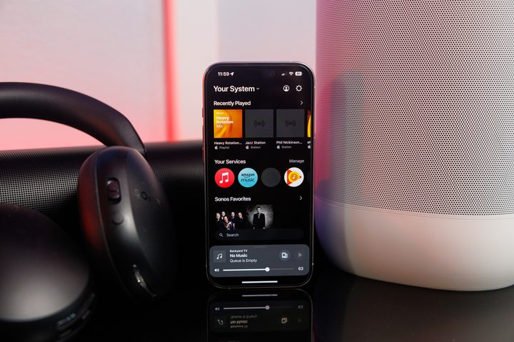 The Sonos app on an iPhone in front of Sonos speakers and headphones.