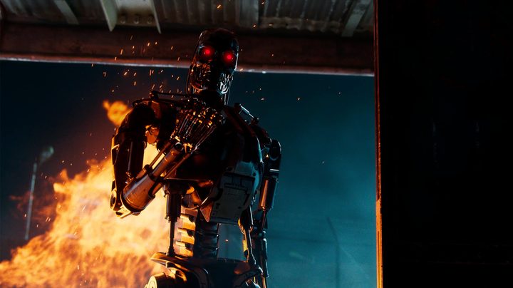 A T-800 holding up its fist in front of flames. Its eyes are glowing red.
