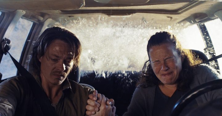 A couple holds hands in a car as a wave crashes into it in The Wave.