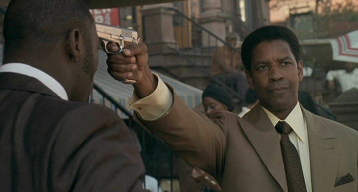 A man points a gun at another man's head in American Gangster.