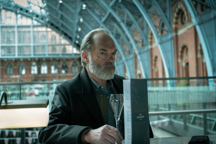 Hugo Weaving sits at a train station bar in Slow Horses season 4.