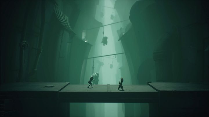 Two smalll figures walk across a narrow bridge as large people hang from hooks in Little Nightmares 3