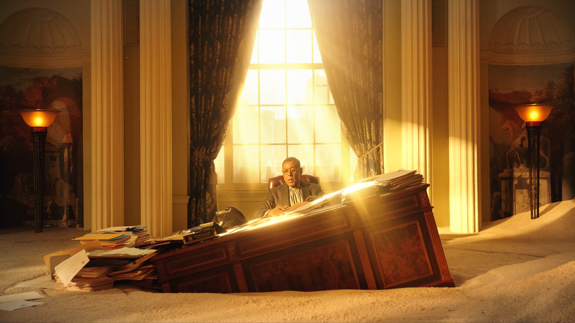 Giancarlo Esposito sits at a desk surreally sinking into sand in a still from the movie Megalopolis.
