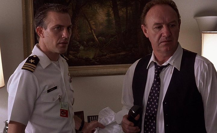 A naval officer and a man in a suit look confused as they stand next to each other.