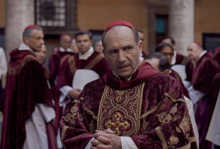 Ralph Fiennes dressed as a pope looks to his left.