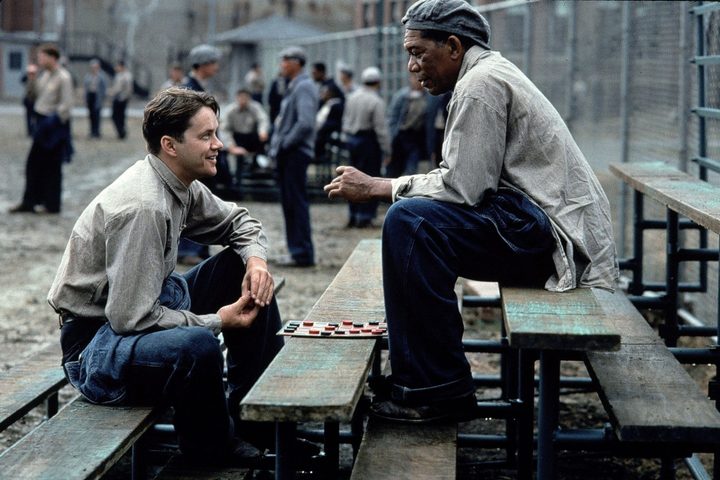 Tim Robbins and Morgan Freeman sit on prison bleachers together in The Shawshank Redemption.